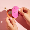 Bright pink and orange leather compact mirror, personalised with a name, modelled in hand - by Sbri