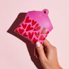 A lady's hand holding a fuchsia pink leather coin purse with red heart pattern and personalised initials