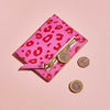 Fuchsia pink leather card holder with red leopard print spots and personalised lettering, shown with coins