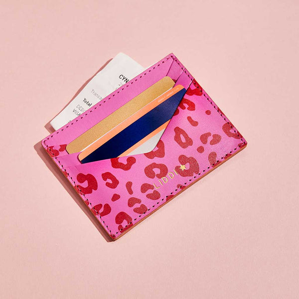 Fuchsia pink leather card holder with red leopard print spots and personalised lettering, shown with bank cards and receipts