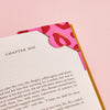 A pink leather bookmark with red leopard print spots, shown on the corner of a page with the personalisation 'Laura'