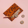 Tan brown leather card holder with leopard print spots and personalised lettering, shown with coins