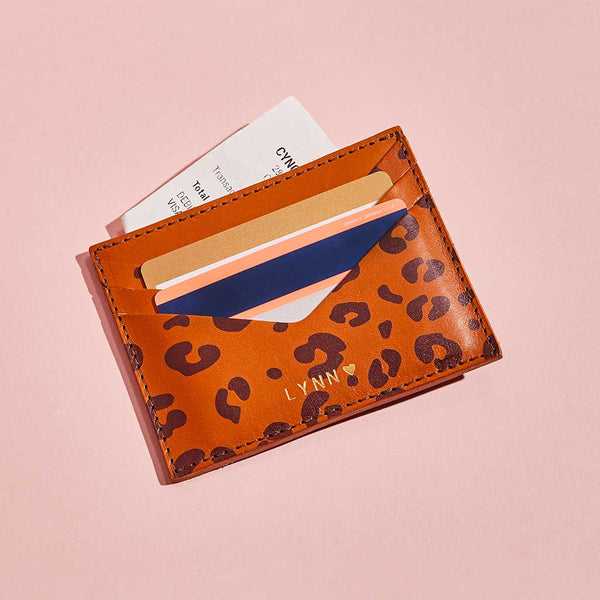 Tan brown leather card holder with leopard print spots and personalised lettering, shown with bank cards and receipts